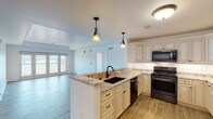 This single-floor residence offers a thoughtfully designed open-concept layout that seamlessly connects the kitchen and living areas. The kitchen serves as the heart of the home, showcasing cream-glazed cabinetry extending to the ceiling with crown molding detail, granite countertops, and a peninsula with a double undermount sink illuminated by decorative pendant lighting. Black stainless steel appliances, including a gas range, over-the-range microwave, dishwasher, and French door refrigerator, complete the culinary space. Wood-look tile flooring runs throughout the main living areas, adding warmth and continuity.

The living area transitions smoothly from the kitchen, with access to a balcony through glass doors that invite natural light. The bedroom features plush carpeting, a ceiling fan, a tray ceiling, and a generous window framing scenic views of a waterway and surrounding landscape.

Two bathrooms mirror the home's refined aesthetic, featuring granite-topped white vanities, marble-look tile flooring, and oil-rubbed bronze fixtures. One bathroom includes a tub-shower combination with sliding glass doors and marble-surround tile. A dedicated utility room with cabinetry, a granite countertop, and a utility sink provides additional functionality. A smart home panel is also conveniently located within the unit.