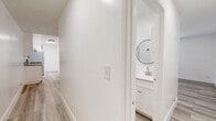 Located at 356 S Rampart Blvd in Los Angeles, CA, this 2-bedroom, 2-bathroom unit offers a well-organized single-floor layout with a bright, clean aesthetic. Light wood-style plank flooring runs consistently throughout, complementing the crisp white walls and textured ceilings found in each room. The open living area benefits from a ceiling fan and flows naturally toward the kitchen, which features a galley-style design with white cabinetry, granite-look countertops, a stainless steel sink, and a skylight that draws in natural light. Appliances include a gas range and refrigerator. The primary bedroom is a well-proportioned space with a window fitted with horizontal blinds and a wall-mounted PTAC unit for climate control. The second bedroom mirrors a similar layout and features a sliding-door closet. Both bedrooms are bright and offer clean, neutral finishes. The two bathrooms are tastefully updated — one includes a tub/shower combo with a white vanity and round mirror, while the second offers a glass-door shower stall with matching vanity and mirror accents. Black hardware details throughout the bathrooms provide a modern contrast to the all-white fixtures and surfaces.