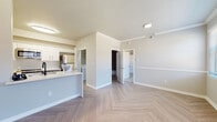 This single-floor residence is designed with a clean, contemporary aesthetic throughout. The open living and kitchen area serves as the heart of the unit, where light-toned herringbone-patterned flooring creates a visually striking foundation. Crown molding and a chair rail add architectural detail to the living space, which is further enhanced by a ceiling fan and ample recessed lighting. A kitchen peninsula with quartz countertops featuring subtle veining provides both workspace and a natural division between the kitchen and living area. The galley-style kitchen is outfitted with white upper cabinetry, gray lower cabinets, matte black hardware, matching quartz countertops on both sides, and stainless steel appliances including a dishwasher and range. An in-unit washer and dryer area is conveniently tucked nearby. The bedrooms feature plush neutral carpet and six-panel doors, with at least one room benefiting from a window that allows natural light. The bathroom includes a single vanity with quartz countertop, a tub-shower combination with tile surround, matte black fixtures, and a lighted mirror. Neutral warm-gray walls are consistent throughout, contributing to a cohesive and modern ambiance.