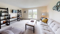 Located at Boulders in Amherst, Massachusetts, this single-floor residence offers a well-organized and functional layout designed for comfortable everyday living. The open-concept living area is carpeted and bathed in natural light through large windows that frame outdoor views, creating a bright and welcoming atmosphere. Adjacent to the living space, a dedicated dining area provides ample room for a full dining table and seating, making it well-suited for shared meals or gatherings. The galley-style kitchen features warm wood cabinetry, white appliances including a range and refrigerator, a double sink, and durable hardwood-style flooring, offering efficient use of space and practical storage throughout. Multiple bedrooms are carpeted and finished in neutral tones, each offering windows for natural light. Bedrooms include sliding-door closets with built-in shelving, providing generous storage. One bedroom is spacious enough to accommodate two twin beds alongside a desk workspace, while others comfortably fit a full or queen bed with additional furnishings. The bathroom includes a vanity with wood cabinetry, a full-sized bathtub with shower, hardwood-style flooring, and a large mirror. Overall, the space presents a clean, neutral aesthetic throughout.
