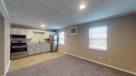 This 1-bedroom, 1-bathroom unit is laid out across a single floor, offering a functional and comfortable living environment. The open-concept main area seamlessly connects the living space and kitchen, with light wood-look flooring in the kitchen transitioning to plush carpeting in the living area. Multiple windows fitted with blinds allow natural light to fill the space, complemented by a wall-mounted air conditioning unit for year-round comfort.

The kitchen is well-appointed with white cabinetry, granite-look countertops, and a full suite of stainless steel appliances, including a refrigerator, range with overhead microwave, and a sink — all set against a textured ceiling with recessed lighting and crown molding accents.

The bedroom is a quiet, carpeted retreat featuring a ceiling fan with light, a window with blinds, and ample wall space, making it easy to customize the layout. The full bathroom includes a tub/shower combo and wood-look tile flooring, keeping the aesthetic cohesive throughout.

Neutral warm-toned walls run throughout the unit, creating a clean and inviting atmosphere that is easy to personalize. The straightforward floor plan, as seen in the 3D overview, maximizes the use of space while maintaining a clear separation between living and sleeping areas.
