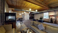 Greystone Lofts offers a thoughtfully designed common area that celebrates its industrial roots while providing a range of resident amenities across a single level. The building's character is immediately established by original exposed brick walls, warm wood-plank ceilings supported by heavy timber beams, and visible ductwork that runs throughout, lending an authentic loft aesthetic to every space.

The main lounge area is generously proportioned, featuring plush seating arrangements anchored around a freestanding stove fireplace, with natural light filtering in through arched and double-hung windows set within the aged brick. An adjacent game room provides a pool table, dartboards, and bar-height seating beneath globe pendant lighting.

A dedicated fitness room is equipped with cardio machines, free weights, and rubber flooring, maintaining the same exposed brick and wood-ceiling aesthetic. The kitchenette includes rich wood cabinetry, dark granite countertops, and a sink, set against a weathered brick backdrop with polished concrete floors.

Accessible ramps and wide corridors connect the various zones, while the welcoming entry features large glass-paned doors, concrete flooring, and a wooden bench. Throughout, the interplay of raw materials and curated furnishings creates an inviting, community-centered atmosphere.