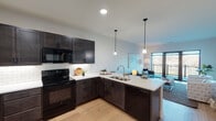 This well-designed single-floor residence offers a thoughtfully arranged open-concept layout that seamlessly connects the kitchen, dining, and living areas. The kitchen is a standout feature, showcasing dark espresso cabinetry with shaker-style doors, white quartz countertops, a classic subway tile backsplash, and a full suite of black appliances including a range, built-in microwave, refrigerator, and dishwasher. A peninsula with an undermount double sink and pendant lighting above bridges the kitchen to the living space, enhancing both functionality and visual flow. Light hardwood flooring runs throughout the main living areas, creating a warm, cohesive aesthetic. The living room is generously sized and bathed in natural light, anchored by large floor-to-ceiling sliding glass doors that open directly onto a private balcony with views of surrounding greenery. The bedroom is a comfortable, carpeted retreat featuring a large window that frames outdoor views and fills the room with natural light. The bathroom is finished with neutral tile flooring, a white vanity with quartz countertop, dark cabinetry, and a full tub-shower combination. Clean lines, neutral tones, and quality finishes throughout give this residence a modern yet inviting character.