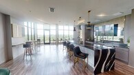 Located at 450 Perimeter Dr in Midlothian, Virginia, this sophisticated amenity space offers a thoughtfully designed, open-plan layout that blends contemporary style with functional versatility. The space is anchored by an expansive floor-to-ceiling window wall that floods the interior with natural light while framing sweeping panoramic views of the surrounding lush, green treetop canopy — a defining feature that carries throughout every area of the space.

At the heart of the space is a dramatic bar and kitchen area, highlighted by a bold, dark stone countertop with striking white veining and a curved accent panel. Gold-toned pendant lights hang above the bar seating, complemented by navy blue leather chairs with brushed gold legs. Wood-toned cabinetry and curated artwork add warmth and visual interest to the backdrop.

An adjacent open lounge area features plush emerald green velvet armchairs arranged around a round white accent table, set atop a bold black-and-white striped rug. Natural light pours in through large windows, creating a relaxed yet refined atmosphere. A separate casual dining zone provides bistro-style high-top tables and bar stools, ideal for informal gatherings. The open-concept layout, warm wood-look flooring, and cohesive modern furnishings throughout create a polished and inviting communal environment.