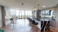 Located at 450 Perimeter Dr in Midlothian, Virginia, this sophisticated amenity space offers a thoughtfully designed, open-plan layout that blends contemporary style with functional versatility. The space is anchored by an expansive floor-to-ceiling window wall that floods the interior with natural light while framing sweeping panoramic views of the surrounding lush, green treetop canopy — a defining feature that carries throughout every area of the space.

At the heart of the space is a dramatic bar and kitchen area, highlighted by a bold, dark stone countertop with striking white veining and a curved accent panel. Gold-toned pendant lights hang above the bar seating, complemented by navy blue leather chairs with brushed gold legs. Wood-toned cabinetry and curated artwork add warmth and visual interest to the backdrop.

An adjacent open lounge area features plush emerald green velvet armchairs arranged around a round white accent table, set atop a bold black-and-white striped rug. Natural light pours in through large windows, creating a relaxed yet refined atmosphere. A separate casual dining zone provides bistro-style high-top tables and bar stools, ideal for informal gatherings. The open-concept layout, warm wood-look flooring, and cohesive modern furnishings throughout create a polished and inviting communal environment.
