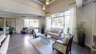This thoughtfully designed single-floor community space blends contemporary elegance with warm, inviting interiors throughout. The main lounge area makes an immediate impression with soaring ceilings, floor-to-ceiling windows draped in patterned linen curtains, and rich dark hardwood floors that run throughout much of the space. Ornate gold pendant light fixtures hang overhead, casting a warm glow across plush seating arrangements that invite relaxation and conversation. Natural light floods the room generously, offering views of the surrounding outdoor environment.

A dedicated waiting area features bold design choices, including deep charcoal accent walls, striking textured wall panels, and eye-catching gold drum pendant lights. Swivel accent chairs arranged around a central ottoman create a stylish and functional seating cluster, while a glass window opens to an adjacent office or reception area.

The fully equipped kitchen features granite countertops, grey cabinetry, a gas cooktop with a stainless steel range hood, and wood-look tile flooring. An intimate lounge nook with a sectional sofa, bistro-style table, and decorative starburst wall art provides a cozy retreat. A central corridor connects all areas seamlessly, with a small dining nook and tasteful artwork completing the refined, cohesive aesthetic of this well-appointed space.