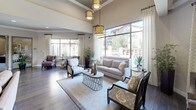 This thoughtfully designed single-floor community space blends contemporary elegance with warm, inviting interiors throughout. The main lounge area makes an immediate impression with soaring ceilings, floor-to-ceiling windows draped in patterned linen curtains, and rich dark hardwood floors that run throughout much of the space. Ornate gold pendant light fixtures hang overhead, casting a warm glow across plush seating arrangements that invite relaxation and conversation. Natural light floods the room generously, offering views of the surrounding outdoor environment.

A dedicated waiting area features bold design choices, including deep charcoal accent walls, striking textured wall panels, and eye-catching gold drum pendant lights. Swivel accent chairs arranged around a central ottoman create a stylish and functional seating cluster, while a glass window opens to an adjacent office or reception area.

The fully equipped kitchen features granite countertops, grey cabinetry, a gas cooktop with a stainless steel range hood, and wood-look tile flooring. An intimate lounge nook with a sectional sofa, bistro-style table, and decorative starburst wall art provides a cozy retreat. A central corridor connects all areas seamlessly, with a small dining nook and tasteful artwork completing the refined, cohesive aesthetic of this well-appointed space.