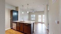 This efficiently designed single-floor unit offers a well-appointed open-concept layout that seamlessly connects the kitchen and living area. The kitchen serves as the centerpiece, anchored by a granite-topped island with a stainless steel undermount sink and pendant lighting above. Dark espresso cabinetry provides ample storage, while the full suite of stainless steel appliances — including a refrigerator, range, microwave, and dishwasher — adds a polished, functional finish. Hardwood-style flooring flows throughout the entire unit, lending warmth and visual continuity. The living area is bright and airy, benefiting from a ceiling fan, recessed lighting, and a pair of French doors that invite natural light and provide outdoor access. A window alongside the French doors further enhances the connection to the outdoors. The bathroom is neatly finished with matching espresso cabinetry, a granite vanity countertop, a toilet, and a glass-enclosed walk-in shower with tile surround and a decorative accent border. A dedicated closet provides practical storage. The neutral color palette and consistent use of quality materials throughout give the space a cohesive, modern aesthetic.