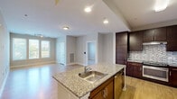 This single-floor, 2-bedroom, 2-bathroom residence is thoughtfully designed to maximize functionality and comfort. The open-concept layout connects the kitchen and living room seamlessly, creating a cohesive and inviting main living area. The kitchen is a standout feature, equipped with rich dark-espresso cabinetry extending to the ceiling, granite countertops, a mosaic tile backsplash, and stainless steel appliances including a range, microwave, and dishwasher. A central island with a built-in sink adds additional workspace and casual dining potential.

The living room benefits from a large bank of windows that invite abundant natural light and offer pleasant outdoor views, complemented by light hardwood-style flooring and track lighting. Both bedrooms are carpeted and include closets, offering comfortable and private retreats. The primary bedroom features a dedicated en-suite bathroom with a walk-in shower, granite vanity, dark cabinetry, and wood-style flooring. The second bathroom includes a soaking tub, tiled flooring, and a granite-topped vanity. Neutral tones and clean finishes throughout contribute to the unit's modern, move-in-ready ambiance.
