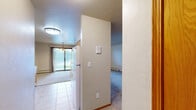Located at 800 Liebman Ct in Green Bay, Wisconsin, this single-floor, one-bedroom, one-bathroom unit offers a practical and comfortable layout. The open living area is carpeted and bathed in a neutral color palette, with baseboard heating running along the walls to ensure warmth during Wisconsin winters. A half-wall partition separates the living space from the kitchen, which features warm wood-tone cabinetry, a light countertop with a built-in sink, and tile flooring — providing both visual distinction and functional separation. The generously sized bedroom is carpeted and includes a window that brings in natural light, a wall-mounted air conditioning unit, and baseboard heating for year-round climate control. Warm wood-trimmed doorways and baseboards throughout add a cohesive, classic touch. The bedroom is served by two closets, one of which is a walk-in with built-in shelving and a hanging rod for ample storage. The bathroom is straightforward and well-appointed, featuring a full tub-shower combination with a curtain rod, tile flooring, and neutral wall tones. A hallway connects the main living areas, completing this efficiently designed, move-in-ready unit.