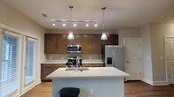 Located at 650 Enterprise Blvd in Charleston, South Carolina, this single-floor property offers a well-designed layout with modern finishes throughout. The kitchen serves as a central highlight of the space, showcasing rich dark wood cabinetry that provides ample storage alongside a clean, light-toned countertop surface. A large central island with a built-in sink and seating area creates a functional and social hub, ideal for both meal preparation and casual dining. Stainless steel appliances, including a gas range, built-in microwave, and a French door refrigerator with an in-door water and ice dispenser, add a sleek, contemporary feel. Stylish pendant lights hang above the island, complementing a multi-bulb track lighting system that ensures the kitchen is well-lit. A neutral tile backsplash ties the cabinetry and countertops together cohesively. The warm hardwood-style flooring extends throughout, adding a sense of continuity and warmth to the interior. The overall ambiance is clean, modern, and functional, reflecting a thoughtfully designed space suited for everyday living in the heart of the Charleston area.