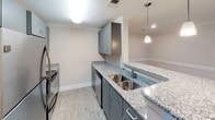 This single-floor residence offers a thoughtfully designed open-concept layout that seamlessly connects the main living areas. The living room is bright and welcoming, finished with warm wood-look luxury vinyl plank flooring, neutral-toned walls, crown molding, and a ceiling fan. A glass door provides access to a balcony, allowing natural light to flow into the space.

The kitchen is a standout feature, showcasing gray cabinetry, granite countertops, and stainless steel appliances including a refrigerator, range, and dishwasher. A peninsula with pendant lighting above serves as both a functional prep area and a casual dining spot, while the open sightlines keep the kitchen connected to the surrounding living space.

The bedroom offers plush carpeting, neutral walls, a ceiling fan with integrated lighting, and a private door for added seclusion. The full bathroom is clean and practical, featuring wood-look flooring, a granite-topped vanity with dark cabinetry, a full tub and shower combination with white surround, and a toilet. Consistent use of granite countertops, gray cabinetry, and light flooring throughout the unit creates a cohesive and modern aesthetic that is both stylish and functional.
