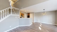 This two-story home offers a well-designed layout with distinct living zones across both floors. The main level showcases an open-concept living and dining area finished with light hardwood-style flooring that flows throughout. A striking geometric pendant light anchors the dining space, while French doors provide access to the outdoors and invite natural light deep into the interior. The kitchen is positioned behind a curved peninsula counter and features warm honey-toned cabinetry with arched detailing, light countertops, and black appliances including a range, microwave, and dishwasher. A staircase with a classic white balustrade connects the main level to the upper floor. Upstairs, a hallway with vaulted ceilings and a ceiling fan leads to multiple carpeted bedrooms, each benefiting from natural light through large windows. The upper level also includes a bathroom with a warm wood vanity, white countertop, and overhead lighting. Throughout both floors, neutral gray wall tones, white trim, and consistent finishes create a cohesive and clean aesthetic. Ceiling fans are present in multiple rooms, contributing to both comfort and functionality across the home.