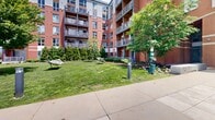 Located along the East Boston waterfront at 126 Border St, this meticulously maintained outdoor space offers direct, unobstructed views of Boston Harbor and the city skyline beyond. The grounds are defined by expansive, well-kept lawns bordered by mature shade trees, neatly trimmed evergreen shrubs, and colorful seasonal flower beds filled with vibrant plantings set in carefully mulched borders.

A paved harborwalk promenade runs along the water's edge, lined with ornamental grasses, flowering perennials, and low bollard lighting, creating an inviting setting for strolling and taking in the panoramic harbor views. A seating area anchored by a circular granite fire pit with Adirondack chairs provides a gathering spot overlooking the water, while freestanding hammocks are positioned across the lawn for relaxed outdoor enjoyment.

At the heart of the grounds, a central courtyard patio features stone planters, outdoor furniture, and a built-in grill area, offering a functional social space framed by the building's red brick facade. The architecture blends contemporary design with classic brick detailing, complemented by balconies at upper levels. Concrete walkways weave throughout, connecting the various outdoor amenity zones seamlessly. The overall ambiance is tranquil, open, and distinctly urban-coastal.