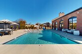 Located at 4418 Oat Grass Circle in Charlotte, NC, this outdoor amenity area serves as a premier community gathering space centered around a generously sized swimming pool with crystal-clear turquoise water. The pool features multiple entry points, including wide steps with in-water lounge chairs that allow residents to relax at the water's edge. Depth markers are clearly visible, and the pool is enclosed by a sturdy wrought-iron fence for added safety and security.

The surrounding deck is finished in a light-toned concrete that reflects the abundant North Carolina sunlight, creating a bright and inviting atmosphere. Ample seating is distributed throughout the space, including sun loungers, shaded dining sets with market umbrellas, and additional casual seating areas suited for both relaxation and socializing.

A standout architectural feature is the adjacent brick clubhouse building, characterized by arched windows, French doors that open directly to the pool deck, a prominent chimney, and a classic design that adds warmth and character to the outdoor setting. A separate modern structure with dark siding provides additional support facilities nearby.

Mature trees and seasonal landscaping frame the perimeter, offering natural privacy and a pleasant backdrop. Under the open blue skies of Charlotte, this outdoor amenity space delivers a resort-style experience for its community residents.
