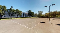 Located at 150 Arbor Cir in Gahanna, Ohio, this outdoor recreational space centers around a well-maintained tennis court that serves as a standout community amenity. The court is finished with a smooth asphalt surface and features clearly marked boundary lines and a regulation net, making it suitable for both casual play and more competitive matches. Tall light poles flank the court, ensuring the space remains functional during evening hours.

Surrounding the court is a verdant landscape of mature trees that provide natural shade and a sense of seclusion, contributing to a peaceful and inviting atmosphere. The greenery is well-kept, enhancing the overall appeal of the outdoor setting. In the background, a multi-story residential building is visible, offering architectural context and illustrating the court's convenient proximity to living spaces.

The open-sky setting allows for abundant natural light throughout the day, and the clear sightlines across the court create a spacious, airy feel. The combination of functional sport infrastructure, lush landscaping, and accessible location makes this court a valuable recreational feature within the community. Whether used for a competitive match or a leisurely rally, the space is designed to encourage an active outdoor lifestyle for its residents.