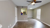 This two-story, 1-bedroom, 1-bathroom home is efficiently designed to maximize functionality across two equally proportioned floors. The main level features warm-toned hardwood-style flooring throughout, a combined dining, kitchen, and living area, and a staircase leading to the upper level. The open-concept living and dining space is brightened by natural light streaming through slatted blinds and is equipped with a ceiling fan. The kitchen features white cabinetry, a stainless steel refrigerator, and is connected to the living area via a convenient pass-through window. A sliding glass door on the main floor provides direct access to the private patio. The staircase, finished with carpet treads and clean white railings, leads to the upper floor where the spacious primary bedroom is located. The bedroom is generously sized with plush carpeting, dual windows allowing ample natural light, and its own ceiling fan. The upper floor also includes two closets and a utility room for added storage and convenience. The full bathroom features white cabinetry with a stone-look countertop, hardwood-style flooring, and a clean, neutral aesthetic. Throughout the home, warm beige walls, white trim, and consistent finishes create a cohesive and inviting atmosphere.