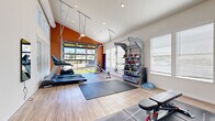 Located in Castle Rock, Colorado, this single-level fitness center is thoughtfully designed to support a wide range of workout routines. The space features soaring vaulted ceilings and a bold terracotta accent wall that energize the room, while light wood-style flooring and abundant natural light from multiple windows and a large glass garage door create a bright, welcoming atmosphere.

The main workout area is generously proportioned, with large interlocking floor mats providing dedicated space for stretching, yoga, or functional training. Cardio equipment includes multiple treadmills and a rowing machine, while strength training is supported by a multi-functional cable and suspension rig complete with TRX straps. A well-organized equipment rack stores medicine balls, kettlebells, and resistance accessories. An adjustable weight bench and a tiered dumbbell rack round out the free weights section.

The glass garage door opens directly to an outdoor turf area, extending the workout space and offering scenic views of the Colorado landscape. Wall-mounted mirrors enhance the sense of openness. A secondary room provides additional exercise space and includes a dumbbell rack and bench, along with access to a restroom area. Recessed lighting and large windows ensure the entire facility remains bright and functional throughout the day.