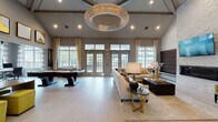 Located at 327 Mill Plain Road in Milford, Connecticut, this single-story amenity facility offers a thoughtfully designed collection of social and wellness spaces. The centerpiece is a generously proportioned lounge and game room characterized by soaring vaulted ceilings, large multi-pane French doors, and an abundance of natural light. A dramatic circular crystal chandelier anchors the space overhead, while light-toned tile flooring, neutral wall tones, and gold-accented furnishings establish a refined, contemporary aesthetic. A full-size billiards table occupies one end of the room, complemented by plush sectional seating and a textured stone accent wall with an integrated media display.

An adjacent wet bar area features sleek dark-wood cabinetry, quartz countertops, under-counter refrigeration, open floating shelves, and a striking geometric tile backsplash. A cozy library nook offers floor-to-ceiling built-in shelving, velvet accent chairs in warm gold tones, and additional decorative display space.

The fitness center is well-appointed with cardio equipment including treadmills and ellipticals, a cable strength-training machine, free weights, and exercise balls. Full-length mirrors visually expand the space, while a dedicated bay-windowed stretching and functional training room with rubberized flooring and outdoor views completes the wellness offering.