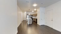 This well-appointed single-floor unit offers a thoughtfully designed open-concept layout that seamlessly connects the living and kitchen areas. Dark hardwood flooring runs throughout the main living spaces, providing a warm contrast to the crisp white walls and ceilings.

The kitchen is a standout feature, equipped with a full suite of stainless steel appliances including a refrigerator, range, microwave, and dishwasher. Taupe wood-grain cabinetry lines the walls, complemented by a classic white subway tile backsplash and light-toned countertops. A central kitchen island offers additional prep and dining space, while pendant lighting above adds a contemporary touch.

The bedroom features large windows that invite natural light and offer views of surrounding greenery, with soft carpeting underfoot. A second room is fitted with wall-to-wall carpet, a ceiling fan, and French doors that open directly to a private outdoor balcony, offering flexible use as a bedroom or living space.

The bathroom is clean and functional, featuring a full tub and shower combination with tile surround, a modern vanity with a white countertop, wood-grain cabinetry, and a large mirror with overhead lighting.

A dedicated laundry room with a full-size washer and dryer, overhead shelving, and a double-door closet rounds out this practical and stylish unit.