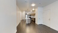 This well-appointed single-floor unit offers a thoughtfully designed open-concept layout that seamlessly connects the living and kitchen areas. Dark hardwood flooring runs throughout the main living spaces, providing a warm contrast to the crisp white walls and ceilings.

The kitchen is a standout feature, equipped with a full suite of stainless steel appliances including a refrigerator, range, microwave, and dishwasher. Taupe wood-grain cabinetry lines the walls, complemented by a classic white subway tile backsplash and light-toned countertops. A central kitchen island offers additional prep and dining space, while pendant lighting above adds a contemporary touch.

The bedroom features large windows that invite natural light and offer views of surrounding greenery, with soft carpeting underfoot. A second room is fitted with wall-to-wall carpet, a ceiling fan, and French doors that open directly to a private outdoor balcony, offering flexible use as a bedroom or living space.

The bathroom is clean and functional, featuring a full tub and shower combination with tile surround, a modern vanity with a white countertop, wood-grain cabinetry, and a large mirror with overhead lighting.

A dedicated laundry room with a full-size washer and dryer, overhead shelving, and a double-door closet rounds out this practical and stylish unit.