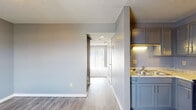 Located at 300 Executive Dr in Newark, Ohio, this two-floor property offers a well-organized layout with a consistent, neutral color palette of soft grays and crisp white trim throughout. The entryway welcomes you with durable light wood-style flooring that extends into the main living corridor, creating a seamless flow between spaces.

The kitchen is thoughtfully equipped with slate-gray cabinetry featuring sleek hardware, light granite-style countertops, a double-basin sink, and a black electric range with an overhead ventilation hood — providing a functional and cohesive workspace. A pass-through hallway connects the kitchen to the rest of the unit, with natural light filtering in from a window at the far end.

The living area is carpeted and features large vertical-blind-covered sliding glass doors that open to an outdoor view, filling the room with generous natural light. Additional carpeted rooms serve as comfortable bedrooms, one of which includes a built-in closet with a hanging rod and shelf for organized storage. A dedicated bedroom also features its own thermostat for climate control.

The bathroom is finished with tile flooring, a wood-toned vanity with a white countertop sink, and wall-mounted lighting above the mirror. Throughout the space, textured ceilings and consistent gray-toned walls lend a clean, uniform aesthetic.