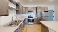 This thoughtfully designed single-floor home on Daylight Drive in Sioux Falls, South Dakota offers a clean, modern aesthetic throughout. The kitchen serves as a functional centerpiece, featuring rich dark-toned cabinetry with gold hardware, light quartz countertops, stainless steel appliances including a refrigerator, electric range, and built-in microwave, a double-basin sink, and a spacious island with additional seating and prep space. Elegant pendant lighting adds a refined touch overhead. The light wood-look flooring flows seamlessly from the kitchen into the open living area, which is bathed in natural light from sliding glass doors that provide direct outdoor access. The bedrooms are comfortably carpeted and include windows overlooking the surrounding neighborhood, offering a bright and airy feel. The primary bathroom is well-equipped with a single-sink vanity featuring dark cabinetry, light countertops, a large mirror, and convenient access to a walk-in closet with wire shelving. A second full bathroom includes a tub-shower combination, a matching vanity, and black accent fixtures. A dedicated laundry area houses a full-size Whirlpool washer and dryer with overhead shelving, adding everyday convenience to this well-appointed home.