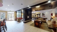 Located at 1055 Pine St in Nashville, TN, this single-floor amenity space offers a well-appointed and multifunctional environment designed for comfort and socializing. The centerpiece of the space is a spacious open lounge anchored by a sleek, double-sided fireplace with a wall-mounted flat-screen TV, surrounded by stylish seating arrangements that include plush sofas, accent chairs, and patterned upholstery in warm earth tones. Large floor-to-ceiling windows flood the interior with natural light and provide views of the outdoor pool and surrounding greenery.

Adjacent to the main lounge is a dedicated game room featuring a full-size pool table and additional lounge seating with a sophisticated dark wood accent wall. A quieter seating nook nearby offers a more intimate setting with coordinated furnishings and curated wall art throughout.

The space also includes a café-style kitchenette with dark cabinetry, a countertop bar with seating, pendant lighting, and a bold red ceiling that adds a vibrant design contrast. A fitness center, visible through glass-paneled doors, is equipped with cardio machines and mirrors. Light-toned tile flooring runs throughout, unifying the space with a clean, modern aesthetic enhanced by recessed lighting and warm accent lamps.