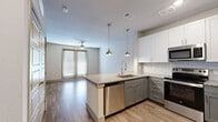 This 1-bedroom, 1-bathroom residence is thoughtfully designed to maximize comfort and functionality. The open-concept layout connects the kitchen and living area seamlessly, creating an inviting and efficient living space. The kitchen is a standout feature, equipped with two-tone cabinetry — white upper cabinets paired with grey lower cabinets — complemented by granite countertops, a subway tile backsplash, and a peninsula island with a built-in sink and pendant lighting above. Stainless steel appliances, including a refrigerator, range, microwave, and dishwasher, complete the modern kitchen. Wood-look flooring extends throughout the main living areas, while the living space benefits from a ceiling fan and access to natural light through large windows with blinds. The bedroom offers plush carpeting, a ceiling fan, a dedicated closet, and a window that allows natural light to filter in. The bathroom features wood-look flooring, a glass-enclosed shower with tiled surround, and a clean, modern aesthetic. Raised panel interior doors and neutral wall tones throughout contribute to a cohesive and contemporary design.