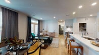 This thoughtfully designed single-floor residence offers a seamless open-concept layout that connects the kitchen, dining, and living areas into one cohesive, light-filled space. Light wood flooring runs throughout the main areas, enhancing the bright and airy atmosphere. The kitchen is a standout feature, showcasing grey shaker-style cabinetry, quartz countertops, a large center island with bar seating, white subway tile backsplash, and stainless steel appliances. A dedicated dining area sits adjacent to the living space, bathed in natural light from a large window dressed with elegant drape panels. The living room is anchored by French doors that open to a private outdoor area, inviting in natural light and fresh air. The bedroom is a serene retreat with plush carpet, a ceiling fan, a generous window, and direct access to the full bathroom. The bathroom features a soaking tub with tiled surround, a single vanity with ample counter space, and a walk-in closet with built-in shelving and hanging storage. A convenient in-unit laundry area with a full-size washer completes this well-rounded and functional home.