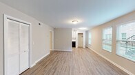 This single-floor unit is designed with a practical, open layout that connects the main living and dining areas seamlessly. The living spaces feature light-toned wood-look flooring, neutral wall colors, and white baseboards, creating a clean and cohesive aesthetic throughout. Natural light filters in through multiple windows fitted with blinds, enhancing the bright, airy feel of the common areas.

The galley-style kitchen is efficiently arranged, offering white cabinetry, a stainless steel sink, and black appliances including a refrigerator, electric range, over-the-range microwave, and dishwasher. Track lighting overhead provides focused illumination, and the layout maximizes available counter and storage space.

The bedrooms are finished with wall-to-wall carpet and include built-in closets with bi-fold doors, offering practical storage. The primary bedroom area connects to an additional room and provides access to the bathroom. The bathroom is straightforward in design, featuring a white vanity with an oval sink, brushed nickel fixtures, a large mirror, and a shower-tub combination. Throughout the unit, flush-mount ceiling light fixtures and HVAC vents are consistently integrated into each room.