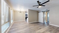 This single-floor residence showcases a clean, modern aesthetic with consistent luxury vinyl plank flooring flowing throughout every room, complemented by neutral warm-beige walls and crisp white baseboards. The open living and dining area is highlighted by two distinct ceiling fixtures — a sleek multi-arm chandelier and a modern black ceiling fan — creating a welcoming, well-lit atmosphere. A standout sliding barn door adds a contemporary design touch, connecting spaces with both style and function.

The kitchen is a galley-style layout outfitted with white shaker cabinetry, matte black hardware, white quartz countertops, a subway tile backsplash, and a full suite of stainless steel appliances including a refrigerator, range, and over-the-range microwave. A coil-style black faucet serves the stainless steel sink, rounding out the thoughtfully curated space.

The bedrooms are generously proportioned, each featuring ceiling fans and windows with horizontal blinds that invite natural light. One bedroom includes a wide sliding-door closet with built-in shelving, offering practical storage. Additional rooms provide flexible use as bedrooms or offices. Throughout the residence, clean lines, consistent finishes, and careful attention to detail create a cohesive, move-in-ready environment.