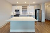 This single-floor unit at 402 Highway 23 NW in Suwanee, Georgia offers a contemporary open-concept layout with modern finishes throughout. The kitchen serves as a central highlight, featuring a large center island with a quartz-style countertop, pendant lighting, white upper cabinetry, gray lower cabinets, a subway tile backsplash, and a full suite of stainless steel appliances including a refrigerator, range, microwave, and dishwasher. The seamless flow between the kitchen and living area creates an inviting, functional space well-suited for both everyday living and entertaining.

The bedroom is bright and airy, benefiting from a natural light-filled window, a ceiling fan, and rich hardwood-style flooring that carries throughout the unit. An adjacent walk-in closet provides generous storage with multiple wire shelving systems and hanging rods for organized use of space.

The bathroom features a soaking tub and shower combination with elegant chevron-patterned gray tile surround, a curved curtain rod, and hardwood-style flooring that complements the overall design palette. The unit's neutral color scheme, recessed lighting, and consistent wood-tone flooring create a cohesive, modern ambiance throughout.