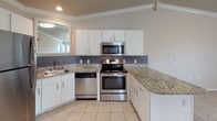 This single-floor residence offers a thoughtfully designed layout with a seamless flow between living and kitchen spaces. The kitchen is a standout area, outfitted with white cabinetry, granite-look countertops, a tile backsplash, and a full suite of stainless steel appliances including a range, over-the-range microwave, dishwasher, and refrigerator. A breakfast bar provides a natural transition into the adjacent living area, which features plush carpeting, crown molding, and a ceiling fan with light fixture. Natural light filters in through windows fitted with blinds, creating a bright and welcoming atmosphere. The bedrooms continue the warm, neutral palette with soft carpeting, ceiling fans, and ample closet space. Vaulted ceilings in one of the bedrooms add an airy sense of openness. The bathroom is cleanly finished with tile flooring, a white vanity with storage, a framed mirror, a tub-shower combination, and well-lit vanity lighting. Throughout the home, consistent use of neutral gray tones, white trim, and tile flooring in wet areas creates a cohesive and move-in-ready aesthetic. Crown molding and ceiling fans are recurring design elements that add a polished touch to each room.