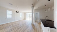 This two-floor home showcases a clean, contemporary design throughout. The main level centers on an open-concept living and dining area finished with light hardwood flooring. A decorative black chandelier anchors the dining space, while a structural column adds architectural character. Multiple windows and glass doors flood the area with natural light and provide access to an outdoor space.

The kitchen is well-appointed with white shaker-style cabinetry, dark countertops, a subway tile backsplash, and stainless steel appliances including a refrigerator, range, and microwave. A peninsula with pendant lighting above offers additional workspace and informal seating. A half bathroom on this level features hardwood flooring and a dark-toned vanity.

Upstairs, the bedrooms are carpeted and include ceiling fans and natural light from windows. One bedroom features a double closet, while another benefits from a spacious walk-in closet with vaulted ceilings and built-in hanging rods. The full bathroom on this level is equipped with a tub-shower combination, brushed nickel fixtures, tile flooring, a recessed medicine cabinet, and a dark vanity.