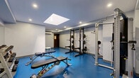 Located at 590 Avenue Outremont in Montréal, this fitness facility is thoughtfully organized across a single level, offering a comprehensive workout experience within a compact footprint. The gym is divided into distinct exercise zones connected by hallways, each serving a specific training purpose.

The strength training area is equipped with dual power racks loaded with Olympic barbells and weight plates, a multi-function cable machine, adjustable workout benches, and a full dumbbell rack ranging across multiple weight increments. A large skylight overhead floods this zone with natural light, complementing the recessed ceiling fixtures for a bright, energizing atmosphere. The clean white walls and vivid blue rubber flooring create a sharp, modern aesthetic throughout.

A dedicated cardio zone features treadmills, upright stationary bikes, and elliptical machines, all lined against a full-length wall mirror that amplifies the sense of space and allows users to monitor their form during workouts. Recessed lighting keeps this area well-lit and functional.

A standout feature of this facility is a traditional wood-panelled sauna, visible in the floor plan, offering a dedicated space for post-workout recovery. The overall design is practical and efficient, making excellent use of the available space while delivering a well-rounded fitness amenity.