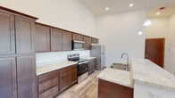 This single-floor residence is designed with an open, airy feel, highlighted by impressively vaulted ceilings throughout that amplify the sense of space in every room. The kitchen is a functional centerpiece, outfitted with rich dark-stained cabinetry extending to the upper reaches of the tall walls, light stone-look countertops, a stainless steel refrigerator, electric range with microwave above, and a double-basin sink set into a peninsula. The flooring in the kitchen features durable wood-look planks that add warmth to the space. The living area is generously proportioned, featuring soft carpeting, a corner fireplace, and a bank of windows that invite abundant natural light and outdoor views. Bedrooms are carpeted and bright, with vaulted ceilings, ceiling fans, and windows that frame exterior views. One bedroom includes access to an adjacent room, offering versatile layout options. The bathroom is cleanly appointed with wood-look flooring, a combination tub and shower unit with grab bars, a toilet, and a modern vanity with a wood cabinet base. The floor plan also accommodates an in-unit laundry area with a stacked washer and dryer. Throughout, neutral tones and consistent finishes create a cohesive and move-in-ready environment.