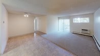 This single-floor unit offers a functional and straightforward layout designed for comfortable everyday living. The open living and dining area is a highlight of the space, featuring a combination of tile flooring and plush wall-to-wall carpeting that defines each zone. A large sliding glass door floods the area with natural light and provides views of the surrounding greenery, while vertical blinds offer privacy and light control. A baseboard heating system runs along the walls, ensuring consistent warmth throughout. A ceiling light fixture anchors the dining area, and the layout flows naturally toward the kitchen, which is visible through an adjoining passage.

The bedrooms are generously proportioned, each finished with soft carpeting and neutral wall tones. Windows dressed with vertical blinds allow natural light to filter in, with one bedroom offering a pleasant outdoor view. Baseboard heaters are present in the bedrooms as well, adding to the unit's efficient heating setup. Textured ceilings are consistent throughout the space.

The bathroom is well-appointed, featuring a wide vanity countertop with an under-mount sink, light wood cabinetry, and a large wall mirror with overhead lighting. A separate tub-and-shower combination with a curtain rod and tile surround completes the bathroom, finished with easy-care tile flooring. Overall, the unit presents a clean, neutral palette ready for personalization.