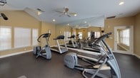 Located at 7609 Kings Ridge Dr in Charlotte, NC, this dedicated fitness center offers a well-organized and fully equipped exercise space designed to support a complete workout routine. The single-floor layout is finished with durable dark rubber flooring throughout, providing both safety and comfort during exercise.

The space is bathed in natural light through multiple white-shuttered windows positioned along the walls, creating a bright and motivating atmosphere. Warm, neutral-toned walls and recessed lighting complement the open feel of the room, while ceiling fans installed throughout promote comfortable air circulation during workouts.

Large floor-to-ceiling mirrors line one wall, visually expanding the space and allowing users to monitor their form during exercise. The cardio section is well-stocked with treadmills and elliptical trainers from Precor, a leading fitness equipment brand. A multi-station cable and weight machine provides options for a wide range of strength-training exercises, while a full dumbbell rack with a comprehensive range of free weights supports targeted muscle training. A wall-mounted television adds entertainment for those logging extended cardio sessions.

The fitness center's thoughtful layout ensures ample space between equipment, allowing multiple users to exercise comfortably and safely at the same time. Overall, this facility delivers a clean, functional, and inviting environment for residents seeking convenient access to quality fitness amenities.