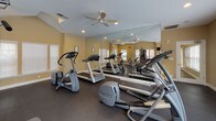 Located at 7609 Kings Ridge Dr in Charlotte, NC, this dedicated fitness center offers a well-organized and fully equipped exercise space designed to support a complete workout routine. The single-floor layout is finished with durable dark rubber flooring throughout, providing both safety and comfort during exercise.

The space is bathed in natural light through multiple white-shuttered windows positioned along the walls, creating a bright and motivating atmosphere. Warm, neutral-toned walls and recessed lighting complement the open feel of the room, while ceiling fans installed throughout promote comfortable air circulation during workouts.

Large floor-to-ceiling mirrors line one wall, visually expanding the space and allowing users to monitor their form during exercise. The cardio section is well-stocked with treadmills and elliptical trainers from Precor, a leading fitness equipment brand. A multi-station cable and weight machine provides options for a wide range of strength-training exercises, while a full dumbbell rack with a comprehensive range of free weights supports targeted muscle training. A wall-mounted television adds entertainment for those logging extended cardio sessions.

The fitness center's thoughtful layout ensures ample space between equipment, allowing multiple users to exercise comfortably and safely at the same time. Overall, this facility delivers a clean, functional, and inviting environment for residents seeking convenient access to quality fitness amenities.
