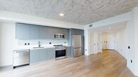Located at 307 SW 5th St in Fort Lauderdale, this contemporary one-bedroom, one-bathroom residence showcases a refined industrial-modern aesthetic throughout. Distinctive exposed concrete ceilings with a textured, marbled finish contrast beautifully against crisp white walls and warm light wood flooring that runs continuously throughout the unit.

The open-concept living area is anchored by floor-to-ceiling sliding glass doors that open to a private balcony, offering expansive elevated views of the Fort Lauderdale cityscape and lush greenery beyond. The kitchen is sleekly designed with flat-front, matte gray cabinetry extending to the ceiling, white countertops, and a full suite of stainless steel appliances including a gas range, microwave, dishwasher, and refrigerator.

The bedroom features large corner windows that flood the space with natural light while framing panoramic city views, accented by a concrete column that adds architectural character. A dedicated walk-in closet with wire shelving and hanging rods provides practical storage.

The bathroom is finished to a high standard, featuring large-format stone-look wall tiles, a frameless glass-enclosed walk-in shower with mosaic tile flooring, a wall-mounted vanity with an illuminated mirror, and modern matte fixtures throughout. Black hardware accents appear consistently across the residence, lending a cohesive, contemporary feel.