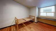 This 130 square foot studio apartment, located in Seattle, WA, exemplifies efficient urban living. The space is thoughtfully designed to maximize functionality within its compact footprint. The main living area features warm hardwood flooring and houses a twin-sized wooden bed frame, providing a cozy sleeping nook.

Adjacent to the bed, a built-in window seat offers a charming spot for reading or enjoying views of the surrounding area. The kitchenette, though small, is well-equipped with a mini-fridge, microwave, and some counter space for basic meal preparation.

A mirrored sliding door cleverly separates the main living space from the bathroom, enhancing the sense of openness. The bathroom, while compact, includes essential fixtures: a toilet, sink with vanity, and presumably a shower (not visible in the images).

The apartment's neutral color palette, dominated by white walls and light wood tones, creates a bright and airy atmosphere. Built-in storage solutions, such as the desk area beneath the window and overhead cabinets, help maintain a clutter-free environment.

This studio is ideally suited for students, young professionals, or anyone embracing a minimalist lifestyle in an urban setting. Its efficient design demonstrates how a small space can be transformed into a functional and comfortable living environment.