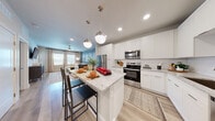 Located at 7551 Narcoossee Rd in Orlando, FL, this thoughtfully designed one-bedroom, two-bathroom residence offers a well-appointed single-floor layout that maximizes both function and style. The open-concept kitchen and living area serves as the heart of the home, where crisp white shaker cabinetry, granite countertops, a subway tile backsplash, and a full suite of stainless steel appliances create a polished culinary space. A central island with seating and stylish pendant lighting adds an inviting gathering spot that flows seamlessly into the living room. The living area is anchored by a striking teal accent wall, ceiling fan, and large windows that invite an abundance of natural light, giving the space an airy, refreshing feel. Light wood-tone flooring runs throughout, enhancing the cohesive and modern aesthetic. The primary bedroom is a serene retreat, featuring natural light from sizable windows with plantation shutters, soft neutral tones, and direct access to a well-designed en-suite bathroom. The bathroom is finished with granite-topped white vanity cabinetry and a tiled walk-in shower. A dedicated closet and a second full bathroom complete this efficiently planned residence, offering comfortable, contemporary living in the heart of Orlando.