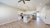 Located in Huntsville, Alabama, this well-appointed single-story home offers a thoughtfully designed open-concept layout that seamlessly connects the kitchen and living area. The kitchen is a standout, featuring crisp white shaker cabinets, granite countertops, a central island with pendant lighting, stainless steel appliances, and a stainless steel French door refrigerator — all set atop durable wood-look luxury vinyl plank flooring that flows throughout the home. Vaulted ceilings and recessed lighting, complemented by a ceiling fan, enhance the airy, bright atmosphere of the main living space. The generously sized primary bedroom includes a ceiling fan, two windows that invite natural light, and direct access to a well-designed en-suite bathroom. The primary bath boasts a dual-sink granite vanity with white cabinetry, matte black fixtures, and framed mirrors. The second bedroom is equally comfortable, with high ceilings and easy access to the hallway. A dedicated closet provides added storage convenience. The attached garage features an automatic opener and a utility panel, adding everyday practicality. Neutral tones and clean, modern finishes throughout create a cohesive and inviting aesthetic.