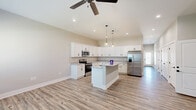 Located in Huntsville, Alabama, this well-appointed single-story home offers a thoughtfully designed open-concept layout that seamlessly connects the kitchen and living area. The kitchen is a standout, featuring crisp white shaker cabinets, granite countertops, a central island with pendant lighting, stainless steel appliances, and a stainless steel French door refrigerator — all set atop durable wood-look luxury vinyl plank flooring that flows throughout the home. Vaulted ceilings and recessed lighting, complemented by a ceiling fan, enhance the airy, bright atmosphere of the main living space. The generously sized primary bedroom includes a ceiling fan, two windows that invite natural light, and direct access to a well-designed en-suite bathroom. The primary bath boasts a dual-sink granite vanity with white cabinetry, matte black fixtures, and framed mirrors. The second bedroom is equally comfortable, with high ceilings and easy access to the hallway. A dedicated closet provides added storage convenience. The attached garage features an automatic opener and a utility panel, adding everyday practicality. Neutral tones and clean, modern finishes throughout create a cohesive and inviting aesthetic.