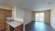 This single-floor residence offers a practical and comfortable layout with a clean, neutral aesthetic throughout. The open-concept living area is a central feature, finished with dark wood-look flooring that extends from the entry door to a sliding glass door fitted with vertical blinds, allowing natural light to fill the space. A ceiling fan with a light fixture adds both function and airflow to the living area.

The kitchen is well-appointed with warm-toned wood cabinetry offering generous storage, granite-style countertops, black appliances including a refrigerator, gas range, and microwave, as well as a sink with a window above. A peninsula counter connects the kitchen to the main living space, enhancing the open flow of the floor plan.

The bedrooms feature soft, neutral carpet and window blinds that provide privacy while allowing natural light to enter. The walls throughout are finished in warm beige tones, creating a cohesive and calming atmosphere.

The bathroom is equipped with wood-look vinyl flooring, a shower-tub combination, a toilet, and a grab bar, offering practical accessibility. Overall, the unit presents a straightforward, well-maintained living environment with consistent finishes across all rooms.