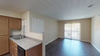 This single-floor residence offers a practical and comfortable layout with a clean, neutral aesthetic throughout. The open-concept living area is a central feature, finished with dark wood-look flooring that extends from the entry door to a sliding glass door fitted with vertical blinds, allowing natural light to fill the space. A ceiling fan with a light fixture adds both function and airflow to the living area.

The kitchen is well-appointed with warm-toned wood cabinetry offering generous storage, granite-style countertops, black appliances including a refrigerator, gas range, and microwave, as well as a sink with a window above. A peninsula counter connects the kitchen to the main living space, enhancing the open flow of the floor plan.

The bedrooms feature soft, neutral carpet and window blinds that provide privacy while allowing natural light to enter. The walls throughout are finished in warm beige tones, creating a cohesive and calming atmosphere.

The bathroom is equipped with wood-look vinyl flooring, a shower-tub combination, a toilet, and a grab bar, offering practical accessibility. Overall, the unit presents a straightforward, well-maintained living environment with consistent finishes across all rooms.