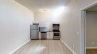 This single-floor unit offers a clean, functional layout with modern finishes throughout. The kitchen is a standout feature, outfitted with a full suite of stainless steel appliances including a refrigerator, dishwasher, electric range, and microwave. White shaker-style cabinetry lines the walls above and below, complemented by a classic white subway tile backsplash that adds a crisp, contemporary touch. A track light fixture and a high clerestory window allow natural light to brighten the space. Light wood-style luxury vinyl flooring runs consistently throughout the unit, tying the rooms together with a warm, cohesive look. The living areas feature neutral gray walls, white baseboards, and textured popcorn ceilings. Each room is equipped with a ceiling fan with integrated lighting, providing both comfort and illumination. Wall-mounted air conditioning units offer independent climate control. Windows fitted with horizontal blinds allow for natural light while maintaining privacy. The entry door opens directly into the main living area, which connects seamlessly to the adjoining rooms. Overall, the unit presents a straightforward, well-maintained interior with practical amenities suited for comfortable everyday living.