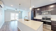 This well-appointed single-story home offers three bedrooms and two full bathrooms across a thoughtfully designed floor plan. The open-concept kitchen and living area serves as the heart of the home, anchored by a large center island with a white quartz countertop, an undermount sink, and brushed gold faucet. Rich dark-espresso cabinetry lines the walls, complemented by stainless steel appliances including a refrigerator, range, microwave, and dishwasher. Pendant lighting over the island adds a modern touch, while the adjoining living area features a ceiling fan and access to the outdoors through French doors that invite natural light. Wood-look plank flooring flows consistently throughout the entire home, creating a cohesive and contemporary feel. The primary bedroom is generously sized, featuring a ceiling fan and French door access to the exterior. The secondary bedrooms are well-proportioned, each with large windows that bring in natural light. Both bathrooms are finished with dark vanity cabinetry, white quartz countertops, brushed nickel hardware, and tub-shower combinations — one featuring classic subway tile accents. A dedicated closet and hallway complete the functional layout of this clean, modern home.