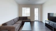 This single-floor unit offers a clean, contemporary design with a neutral color palette and dark hardwood-style flooring that runs consistently throughout the space. The living area is comfortably sized, featuring a large sectional sofa, a glass coffee table, and access to an outdoor balcony through a glass-paneled door. A window fitted with horizontal blinds allows natural light to fill the room, creating a bright and welcoming atmosphere.

The kitchen is well-equipped with stainless steel appliances, including a refrigerator, electric range, and over-the-range microwave. Two-toned cabinetry pairs white upper cabinets with dark lower cabinets, complemented by granite countertops and a double basin sink. Pendant lighting adds a functional decorative touch above the counter.

The unit includes two bedrooms, each furnished with a bed frame, dresser, and desk, with ceiling fans and windows fitted with blinds providing natural views. One bedroom features an adjoining walk-in closet. Both bathrooms are identically appointed with a tub-shower combination, white tile surround, granite-topped dark vanity, and wood-style flooring, maintaining a cohesive aesthetic throughout the unit.